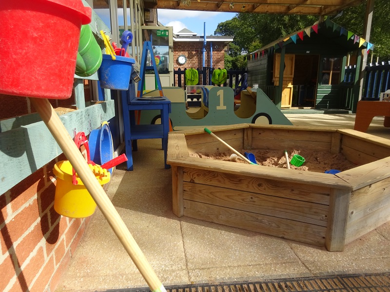Another view of the outdoor area, with the sandpit, racing car and little house.